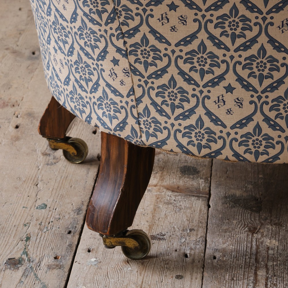 A mid-19th century Victorian upholstered armchair featuring blue and cream patterned fabric, deep button-tufted backrest, turned wooden front legs, and brass castors. View X
