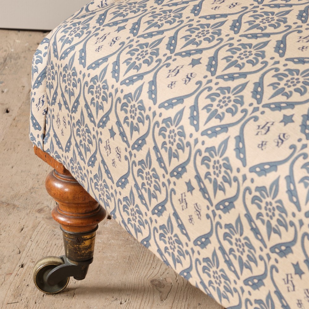 A mid-19th century Victorian upholstered armchair featuring blue and cream patterned fabric, deep button-tufted backrest, turned wooden front legs, and brass castors. View XI