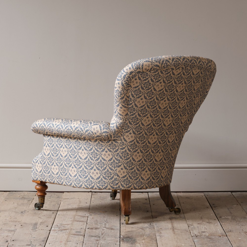 A mid-19th century Victorian upholstered armchair featuring blue and cream patterned fabric, deep button-tufted backrest, turned wooden front legs, and brass castors. View XII