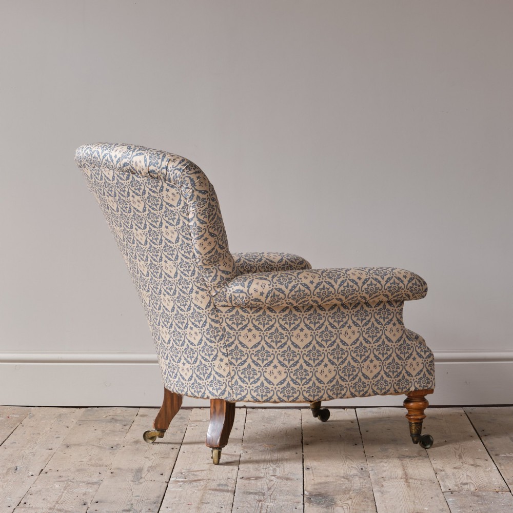 A mid-19th century Victorian upholstered armchair featuring blue and cream patterned fabric, deep button-tufted backrest, turned wooden front legs, and brass castors. View XIV