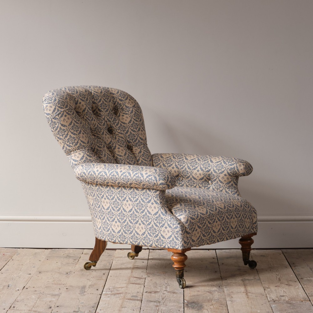 A mid-19th century Victorian upholstered armchair featuring blue and cream patterned fabric, deep button-tufted backrest, turned wooden front legs, and brass castors. View XV