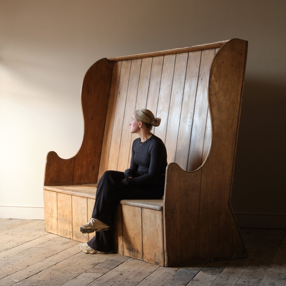 An early nineteenth-century Georgian pine high-backed settle featuring winged side panels and a planked box base.