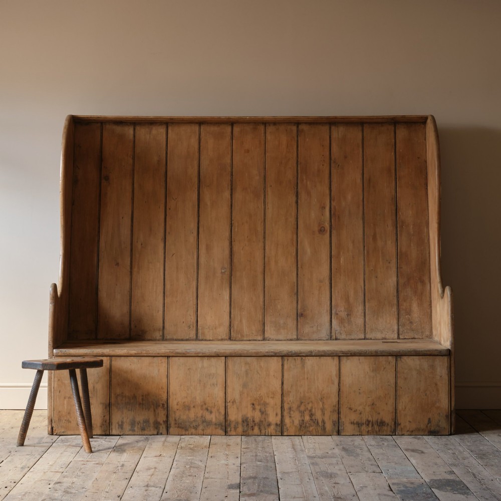 An early nineteenth-century Georgian pine high-backed settle featuring winged side panels and a planked box base. View II