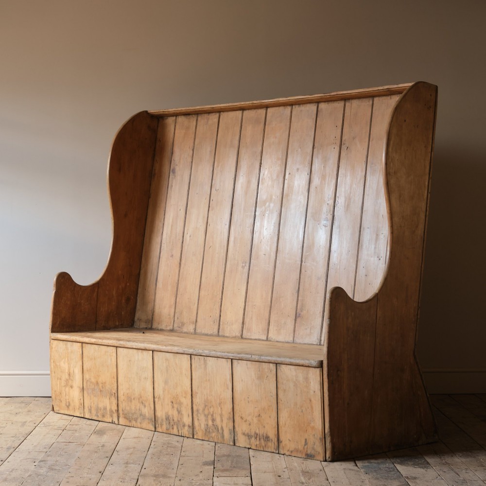 An early nineteenth-century Georgian pine high-backed settle featuring winged side panels and a planked box base. View V