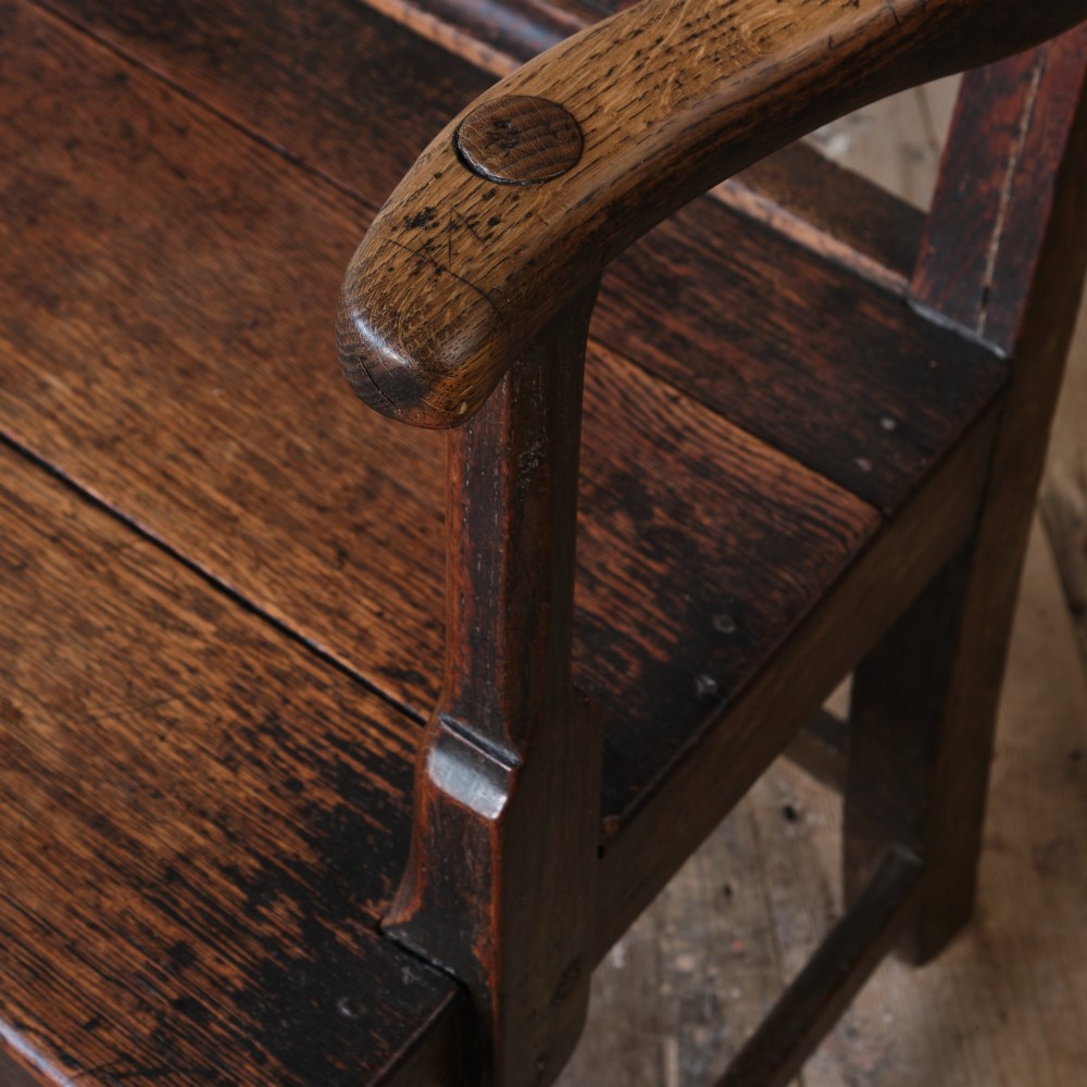 A Georgian oak open armchair featuring a vase-shaped splat back, solid seat, shaped armrests, and an H-stretcher base. View II