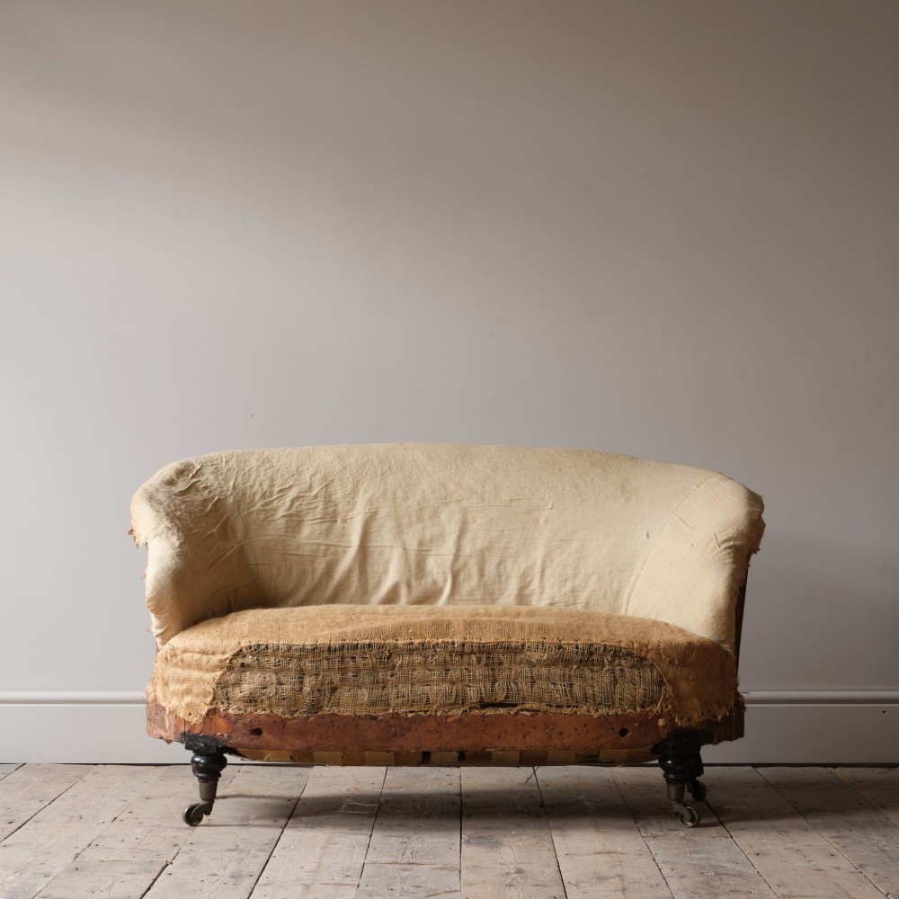 Mid-19th century Victorian Howard & Sons curved-back sofa stripped to its calico and hessian under-upholstery with turned front legs on brass castors. View II