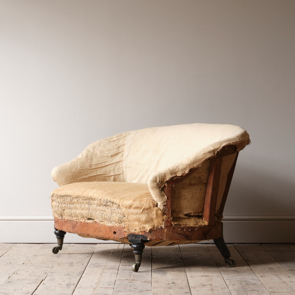 Mid-19th century Victorian Howard & Sons curved-back sofa stripped to its calico and hessian under-upholstery with turned front legs on brass castors. View III