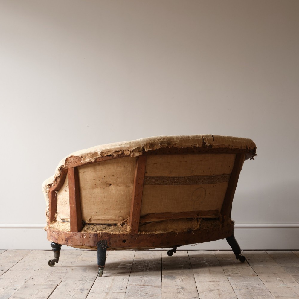 Mid-19th century Victorian Howard & Sons curved-back sofa stripped to its calico and hessian under-upholstery with turned front legs on brass castors. View V