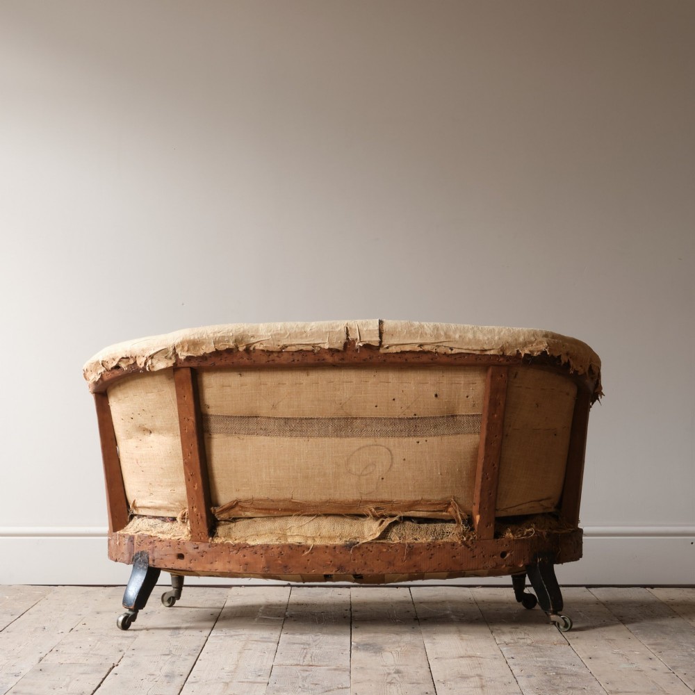 Mid-19th century Victorian Howard & Sons curved-back sofa stripped to its calico and hessian under-upholstery with turned front legs on brass castors. View VI
