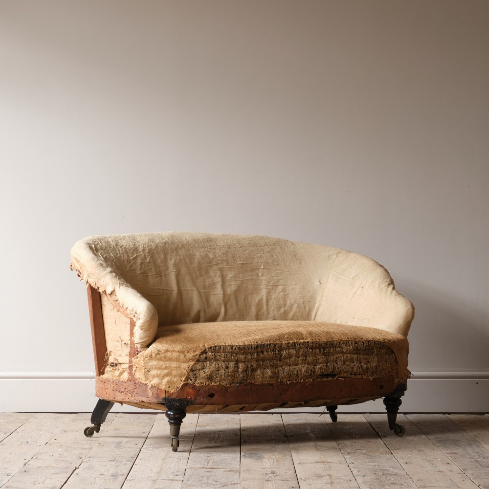 Mid-19th century Victorian Howard & Sons curved-back sofa stripped to its calico and hessian under-upholstery with turned front legs on brass castors. View IX