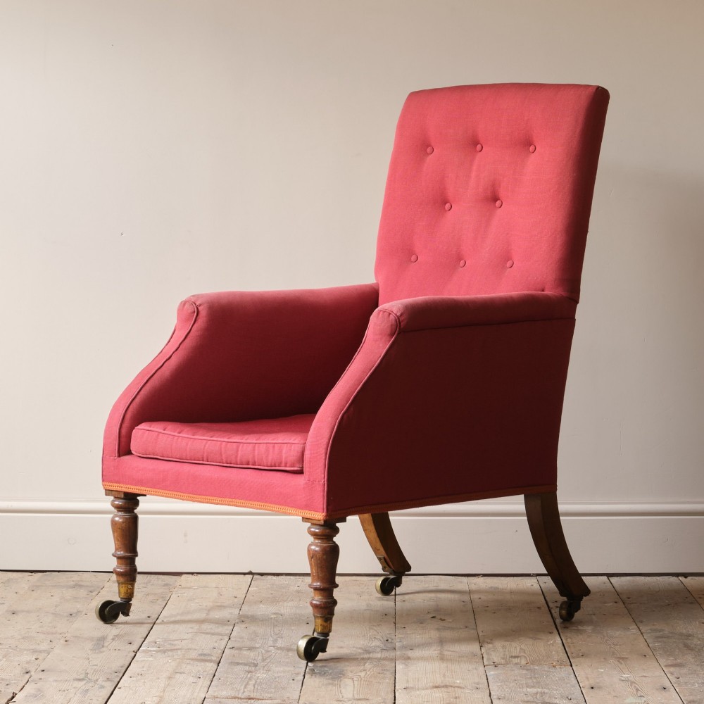 An early 19th-century armchair upholstered in red cloth fabric, featuring a buttoned backrest, padded armrests, and turned timber front legs fitted with brass castors. View II