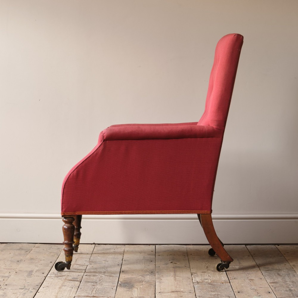 An early 19th-century armchair upholstered in red cloth fabric, featuring a buttoned backrest, padded armrests, and turned timber front legs fitted with brass castors. View III