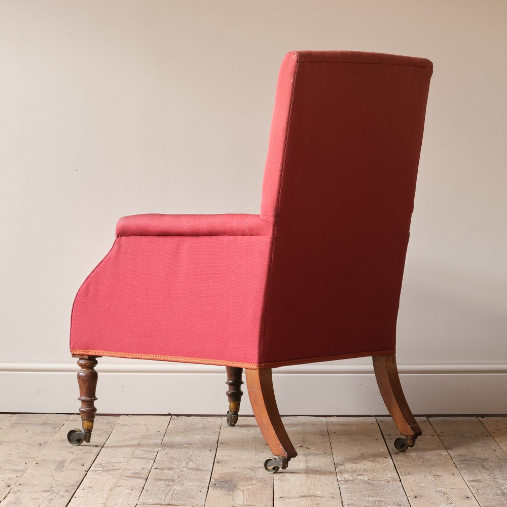 An early 19th-century armchair upholstered in red cloth fabric, featuring a buttoned backrest, padded armrests, and turned timber front legs fitted with brass castors. View IV