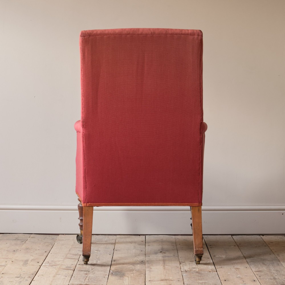 An early 19th-century armchair upholstered in red cloth fabric, featuring a buttoned backrest, padded armrests, and turned timber front legs fitted with brass castors. View V
