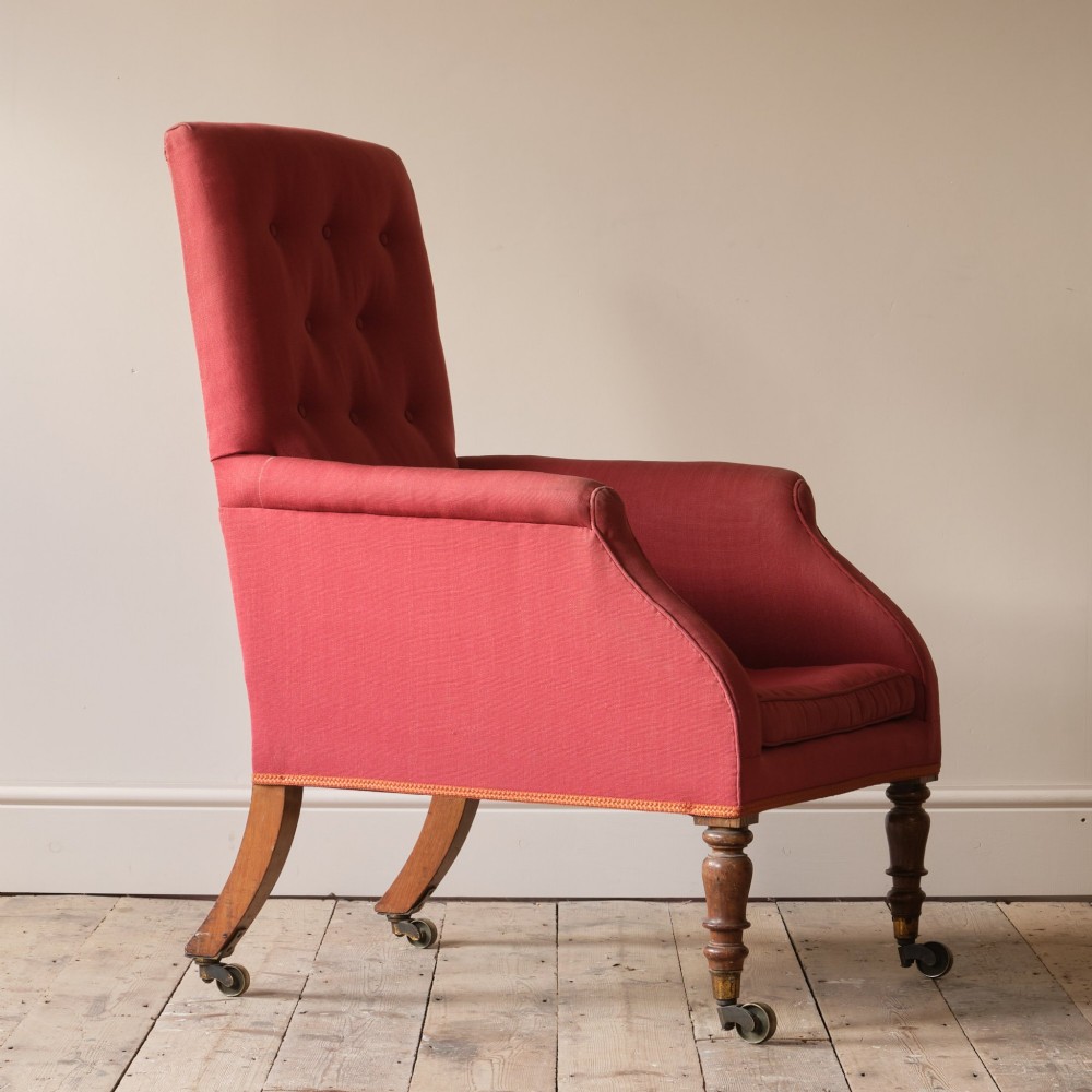 An early 19th-century armchair upholstered in red cloth fabric, featuring a buttoned backrest, padded armrests, and turned timber front legs fitted with brass castors. View VI