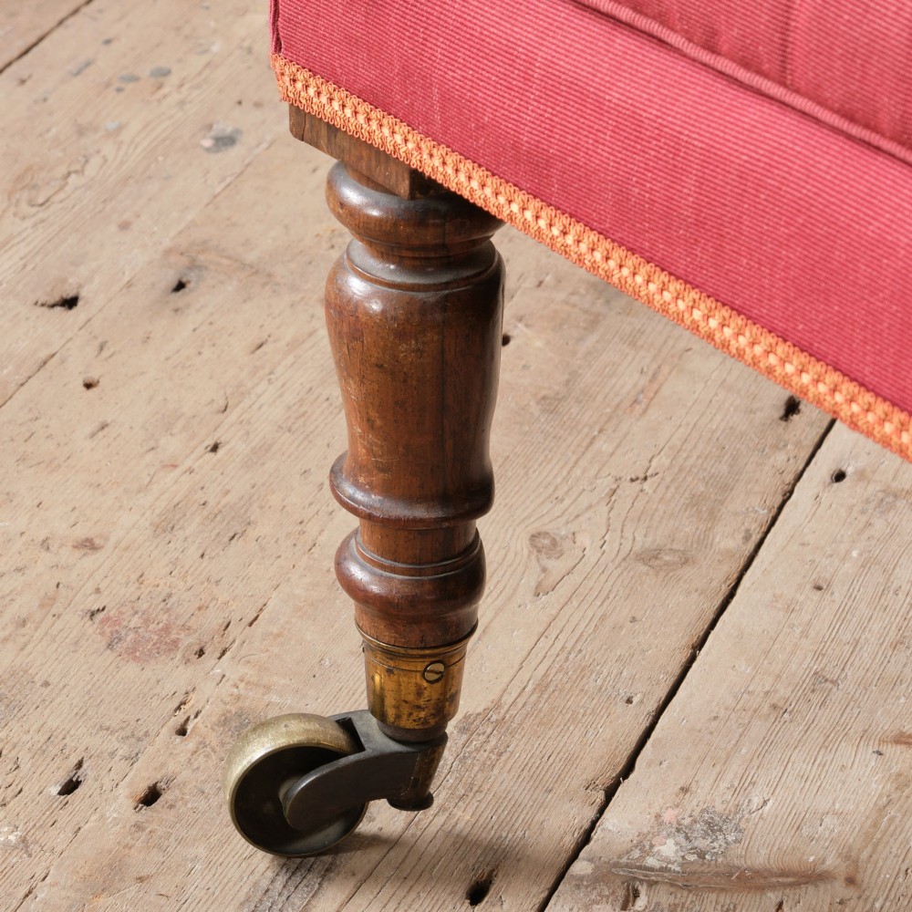 An early 19th-century armchair upholstered in red cloth fabric, featuring a buttoned backrest, padded armrests, and turned timber front legs fitted with brass castors. View VIII