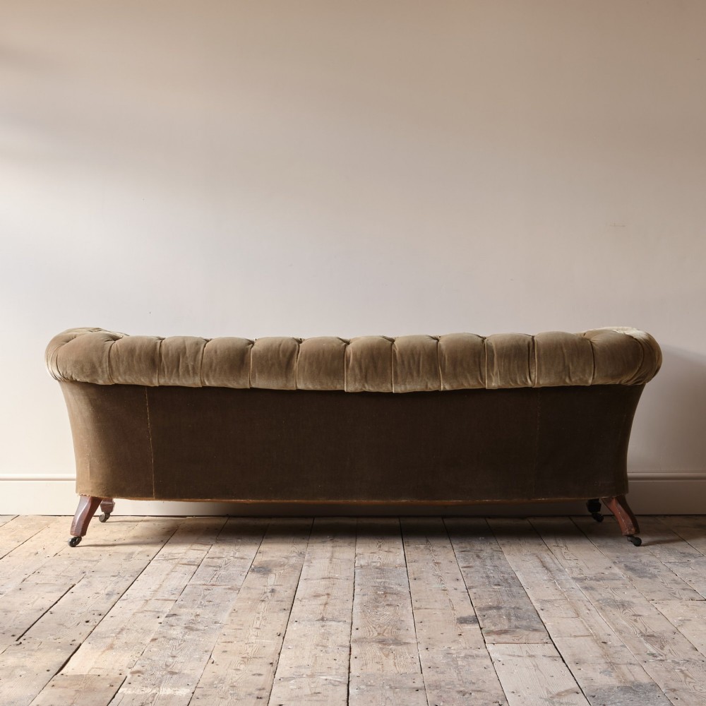 A Victorian Chesterfield sofa upholstered in deep-buttoned olive green velvet with rolled arms and turned legs on castors. View II