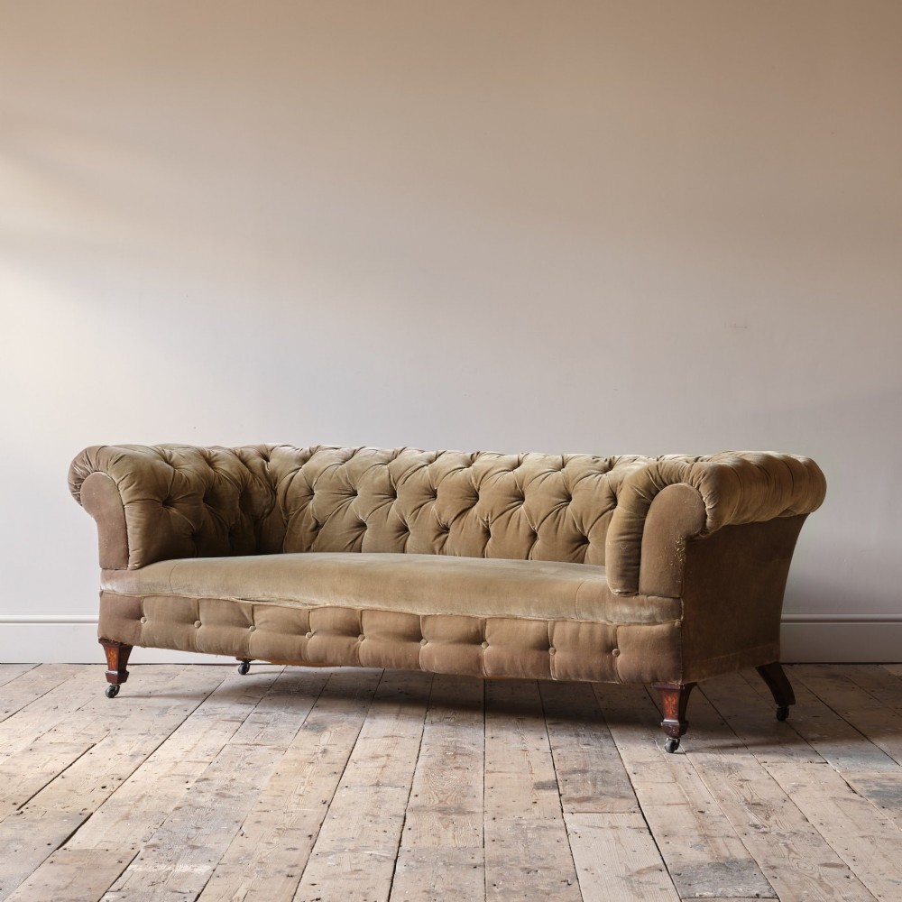 A Victorian Chesterfield sofa upholstered in deep-buttoned olive green velvet with rolled arms and turned legs on castors. View IV