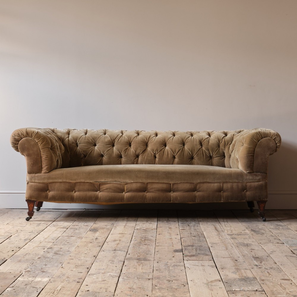 A Victorian Chesterfield sofa upholstered in deep-buttoned olive green velvet with rolled arms and turned legs on castors. View V