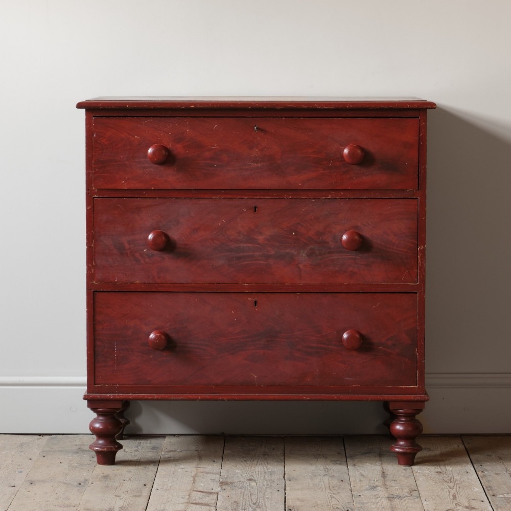 A 19th-century red painted pine chest of three drawers with wooden knob handles and turned feet.
