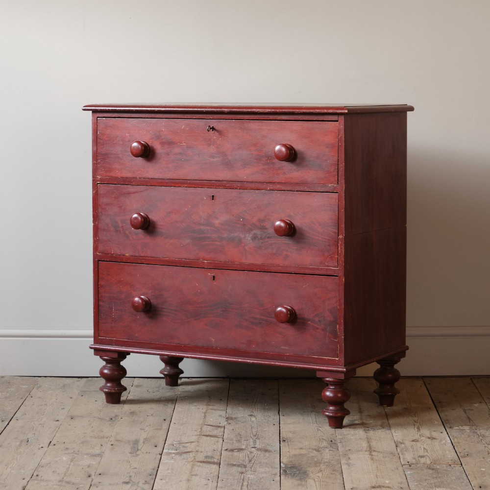 A 19th-century red painted pine chest of three drawers with wooden knob handles and turned feet. View II