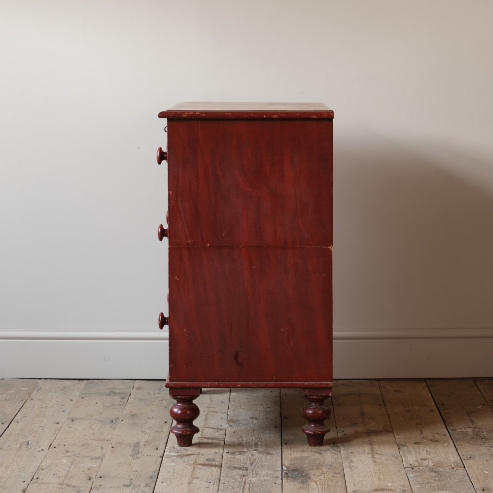A 19th-century red painted pine chest of three drawers with wooden knob handles and turned feet. View III