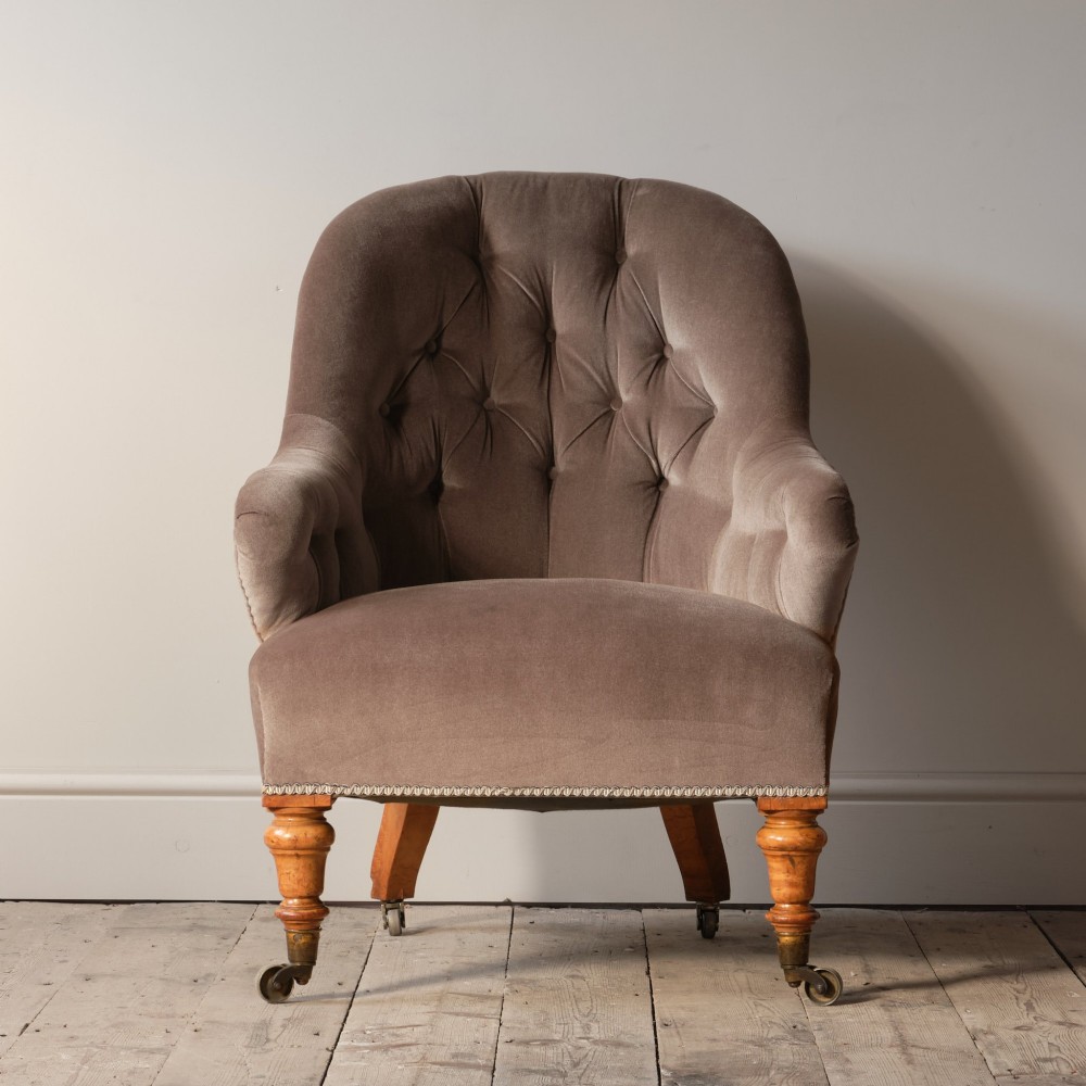 A mid-19th-century button-backed armchair upholstered in taupe velvet with turned timber front legs resting on brass castors.