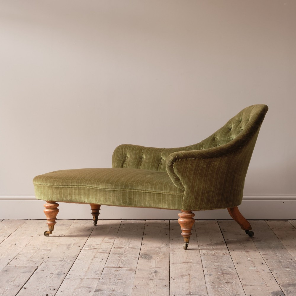 An Early Victorian chaise longue upholstered in olive green velvet with a button-backed finish, supported by turned wooden legs on brass castors.