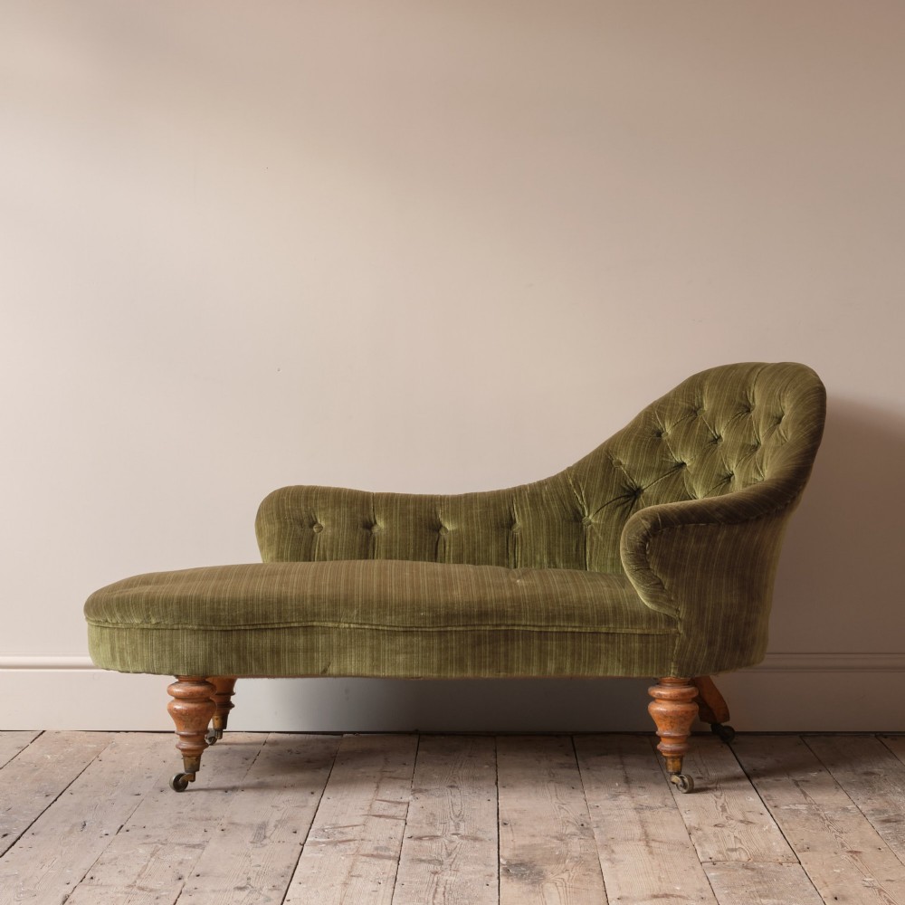 An Early Victorian chaise longue upholstered in olive green velvet with a button-backed finish, supported by turned wooden legs on brass castors. View II