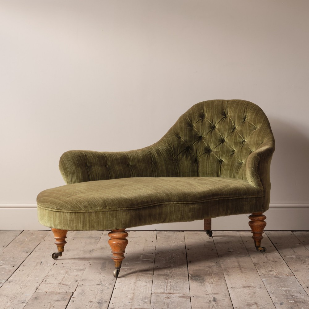 An Early Victorian chaise longue upholstered in olive green velvet with a button-backed finish, supported by turned wooden legs on brass castors. View III