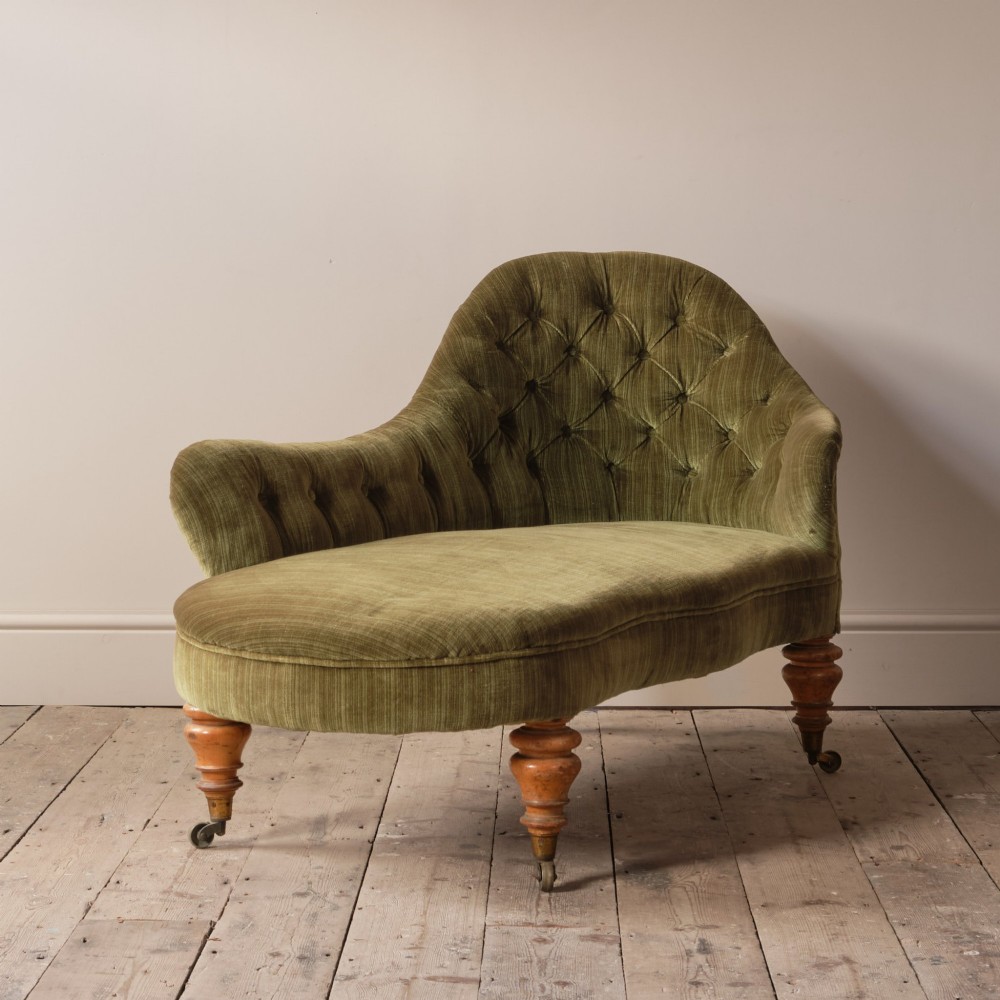 An Early Victorian chaise longue upholstered in olive green velvet with a button-backed finish, supported by turned wooden legs on brass castors. View IV