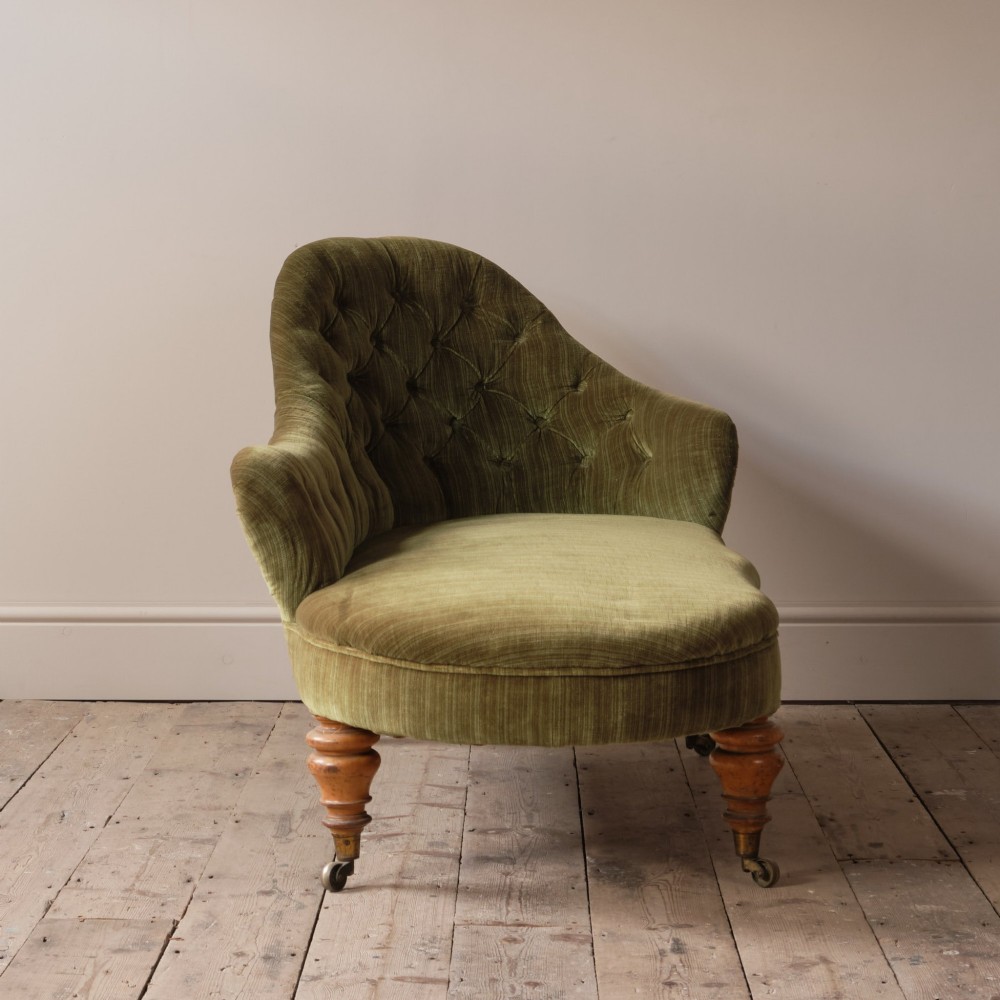 An Early Victorian chaise longue upholstered in olive green velvet with a button-backed finish, supported by turned wooden legs on brass castors. View V