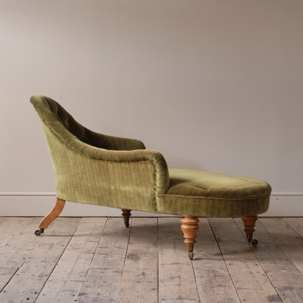 An Early Victorian chaise longue upholstered in olive green velvet with a button-backed finish, supported by turned wooden legs on brass castors. View VI