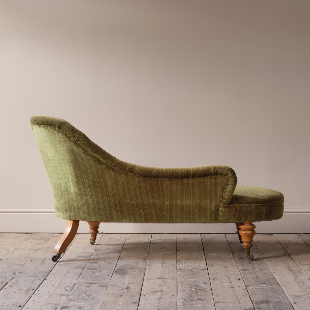 An Early Victorian chaise longue upholstered in olive green velvet with a button-backed finish, supported by turned wooden legs on brass castors. View VII