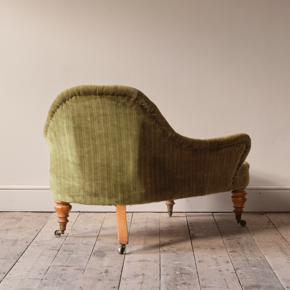 An Early Victorian chaise longue upholstered in olive green velvet with a button-backed finish, supported by turned wooden legs on brass castors. View VIII