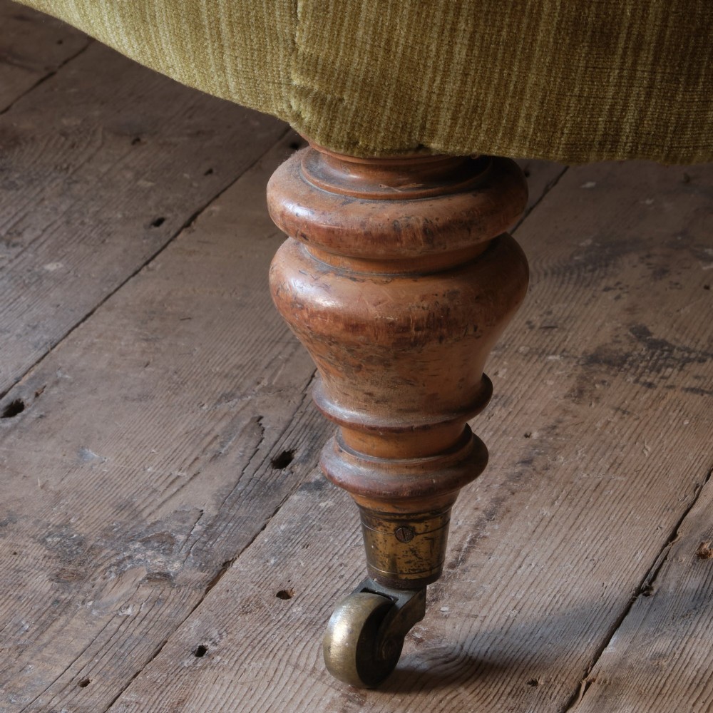An Early Victorian chaise longue upholstered in olive green velvet with a button-backed finish, supported by turned wooden legs on brass castors. View XI