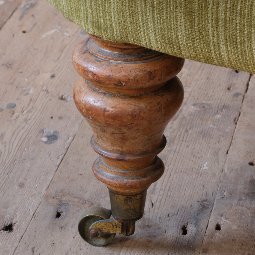 An Early Victorian chaise longue upholstered in olive green velvet with a button-backed finish, supported by turned wooden legs on brass castors. View XII