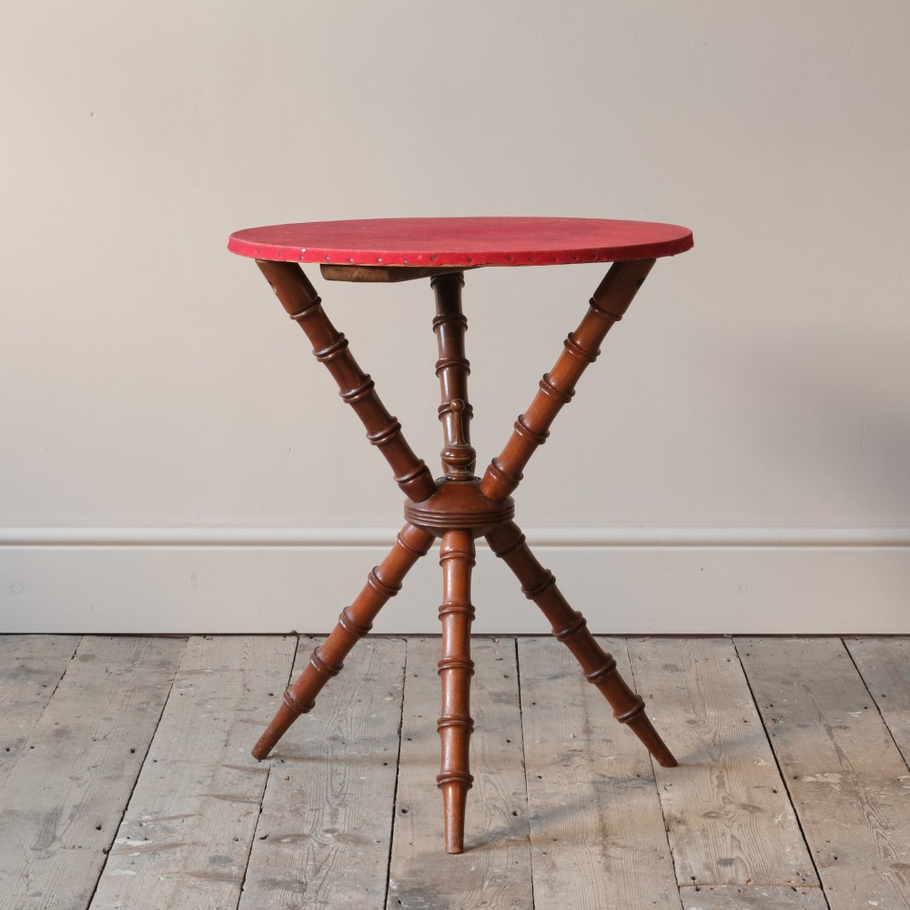 A Victorian faux bamboo walnut gypsy table featuring a circular red fabric-covered top secured with studs and supported by turned tripod legs.