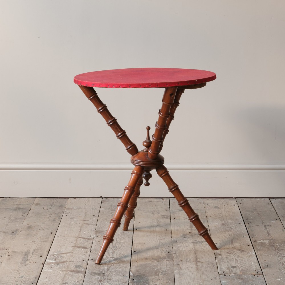 A Victorian faux bamboo walnut gypsy table featuring a circular red fabric-covered top secured with studs and supported by turned tripod legs. View III