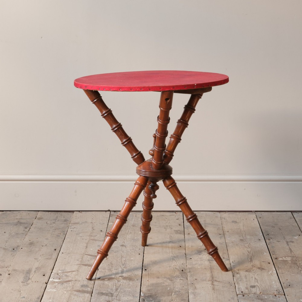 A Victorian faux bamboo walnut gypsy table featuring a circular red fabric-covered top secured with studs and supported by turned tripod legs. View IV