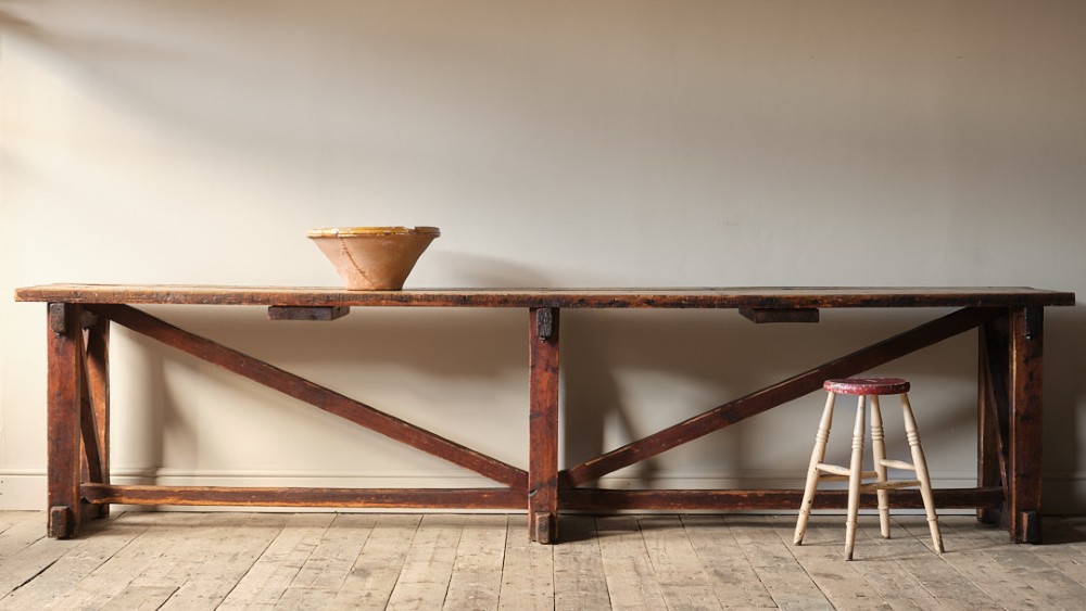 A long antique pine workbench table featuring a heavy plank top supported by a sturdy timber frame with X-frame cross bracing. View II