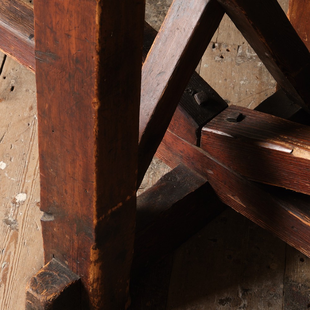 A long antique pine workbench table featuring a heavy plank top supported by a sturdy timber frame with X-frame cross bracing. View III