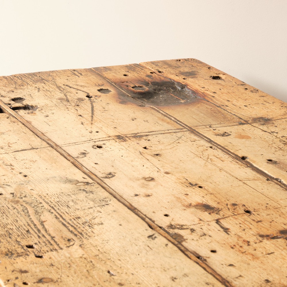 A long antique pine workbench table featuring a heavy plank top supported by a sturdy timber frame with X-frame cross bracing. View V