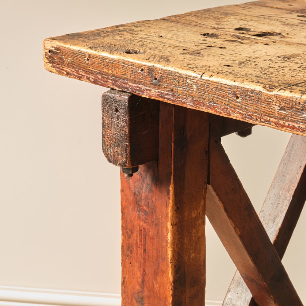 A long antique pine workbench table featuring a heavy plank top supported by a sturdy timber frame with X-frame cross bracing. View VIII