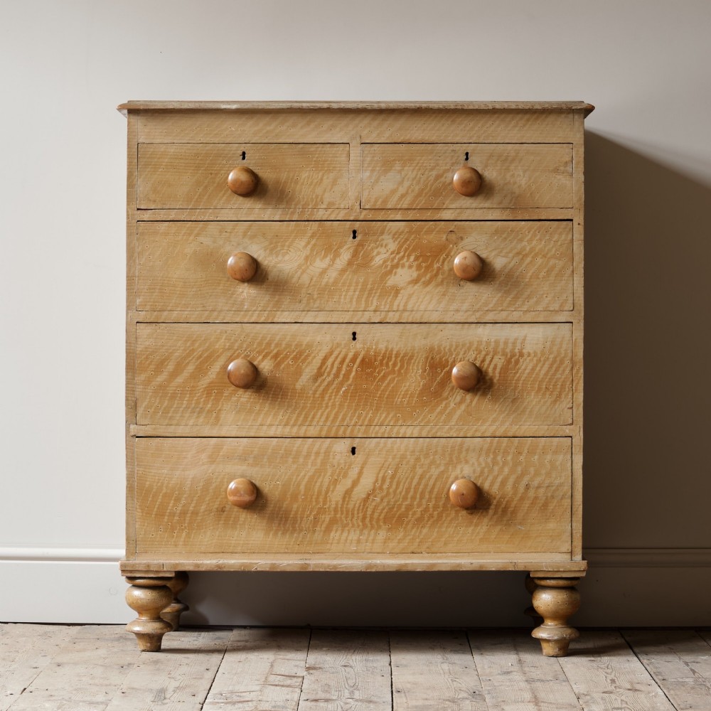 A mid-nineteenth-century pine chest of drawers featuring a faux-grain painted finish, turned wooden knobs, two short drawers over three long drawers, and turned feet.