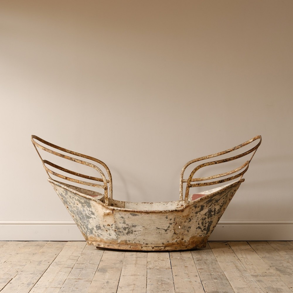 A weathered painted metal fairground swing boat featuring a red wooden seat, riveted sheet body, and curved iron safety rails. View II