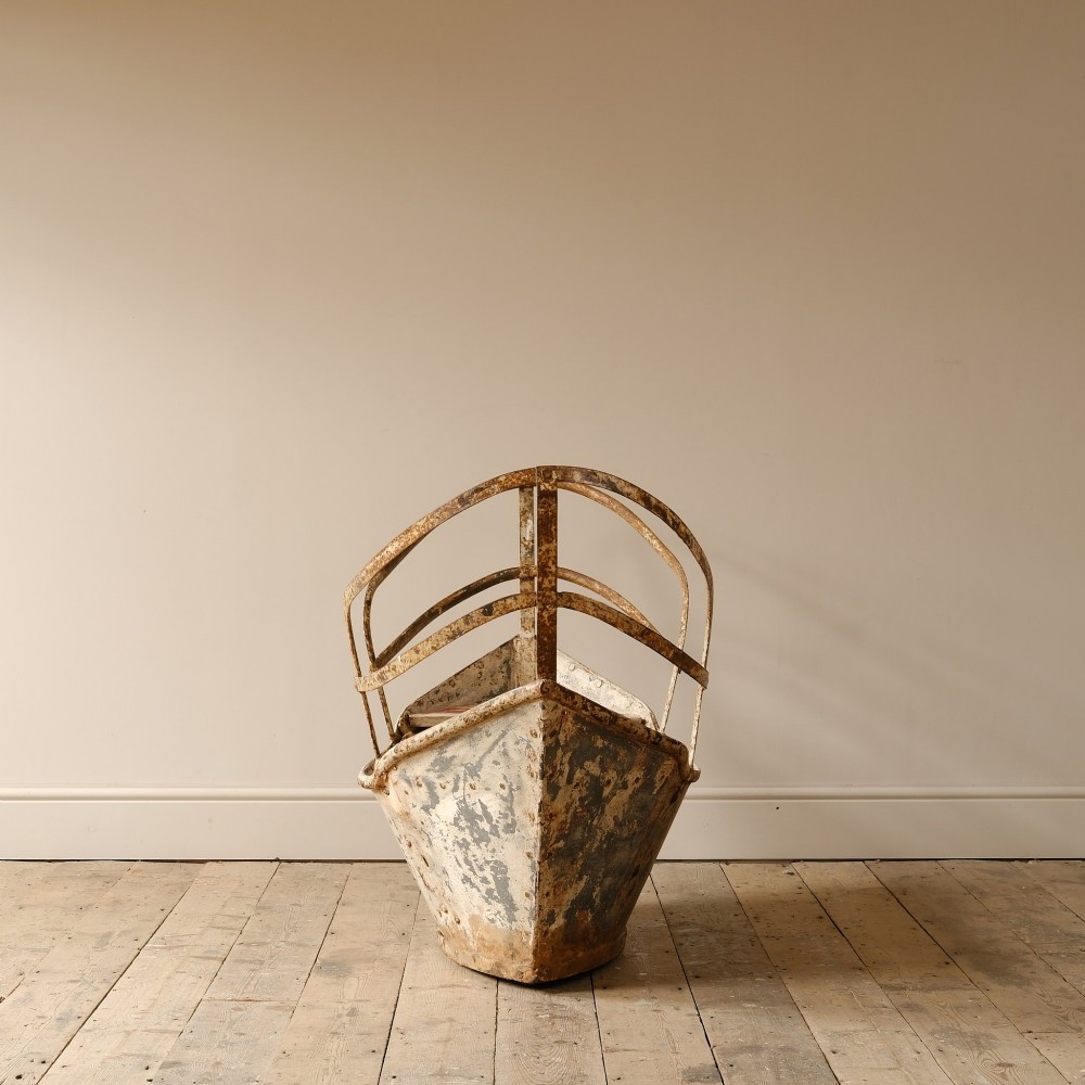A weathered painted metal fairground swing boat featuring a red wooden seat, riveted sheet body, and curved iron safety rails. View V