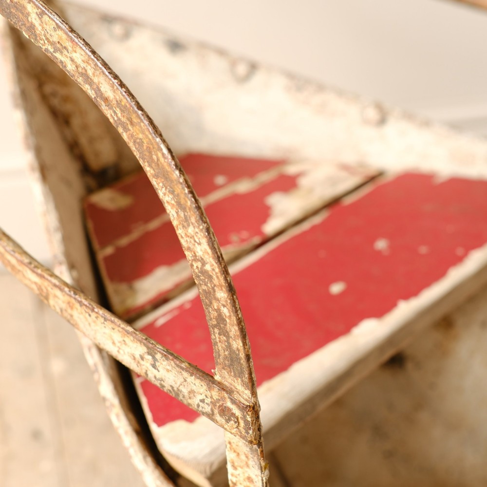 A weathered painted metal fairground swing boat featuring a red wooden seat, riveted sheet body, and curved iron safety rails. View VIII