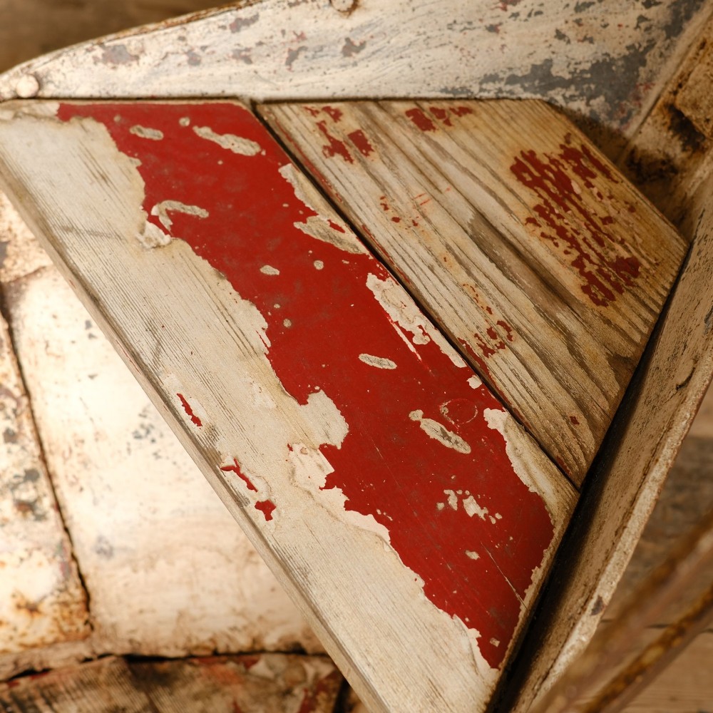 A weathered painted metal fairground swing boat featuring a red wooden seat, riveted sheet body, and curved iron safety rails. View IX