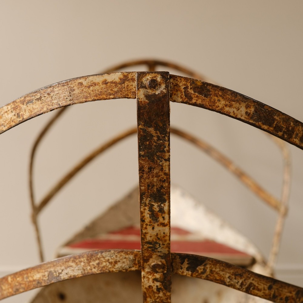 A weathered painted metal fairground swing boat featuring a red wooden seat, riveted sheet body, and curved iron safety rails. View XI